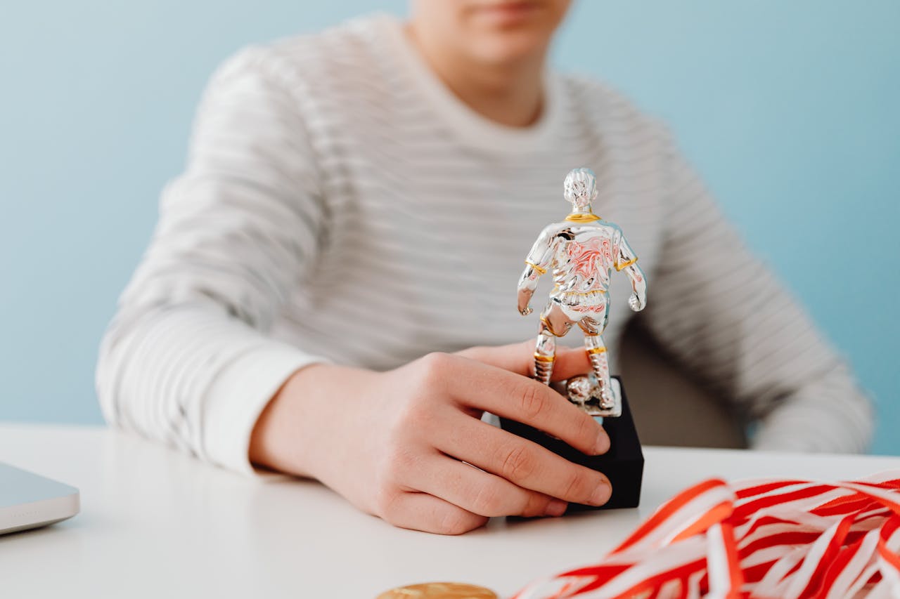 Boy holding a silver football player figurine on a desk with ribbons, signifying achievement.